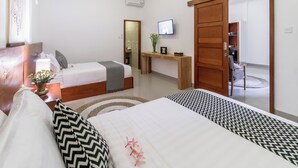 A hotel room with two beds, a TV, a wooden desk, and a sliding door to the bathroom. - Puri Uma Ratu (Keroboken Kelod)