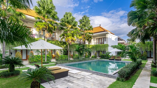 A pool area with lounge chairs, palm trees, and a well-maintained lawn. - Puri Uma Ratu (Keroboken Kelod)