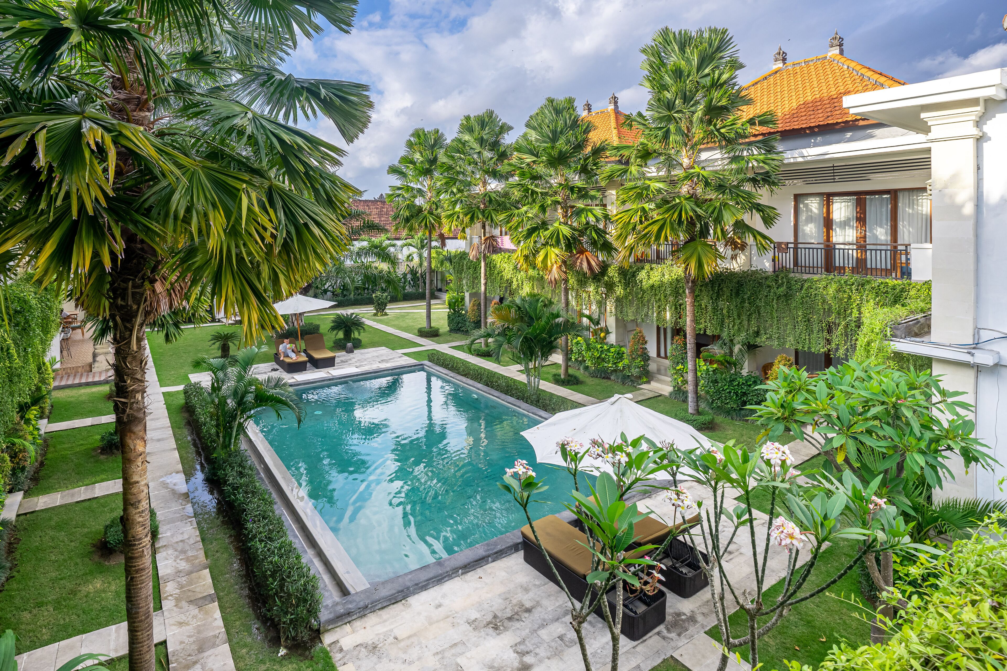 A swimming pool surrounded by palm trees and a well-maintained garden, with a house in the background.