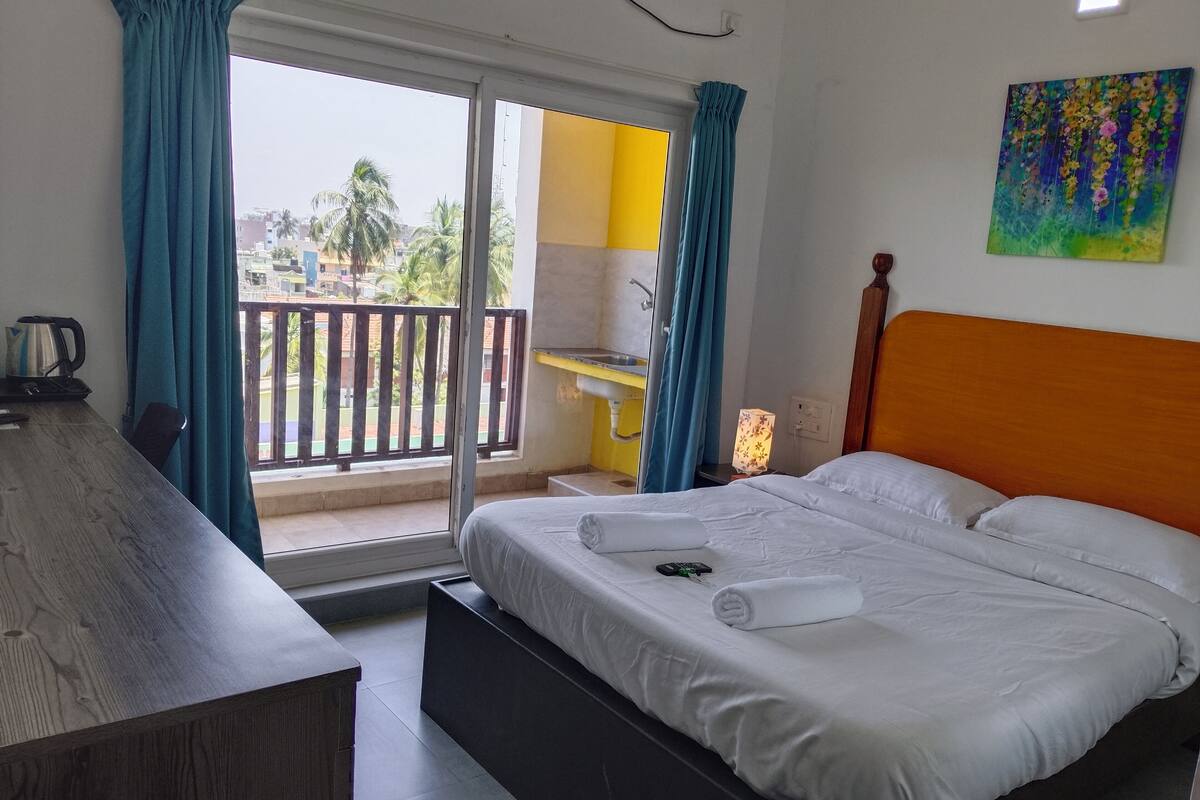 A hotel room with a bed, a desk, a chair, a coffee maker, and a view of the outside.