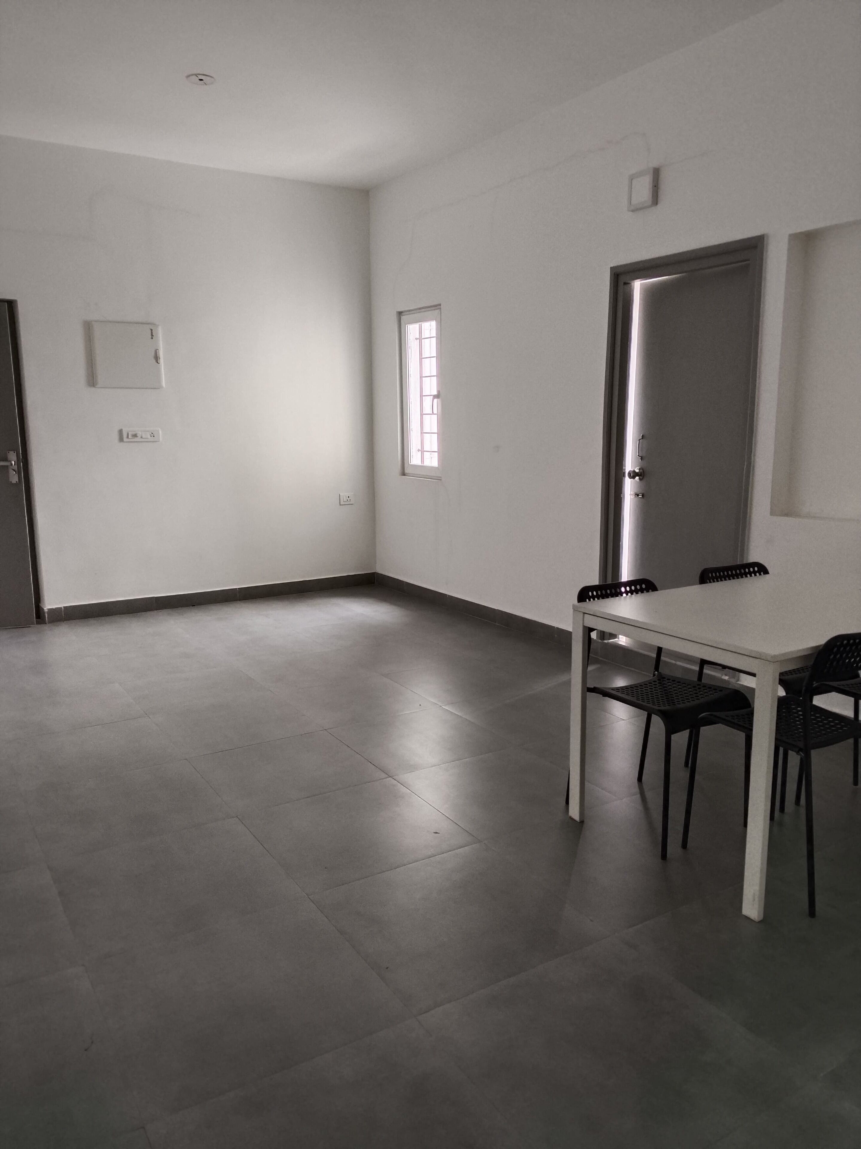 Una habitación con suelo de baldosas, una mesa blanca con cuatro sillas, una puerta y una ventana.
