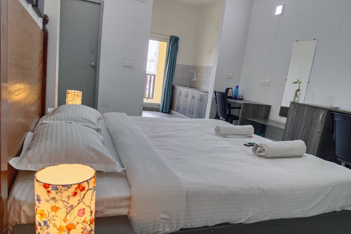 A hotel room with a large bed, a bedside lamp, a mirror, and a view of the bathroom.