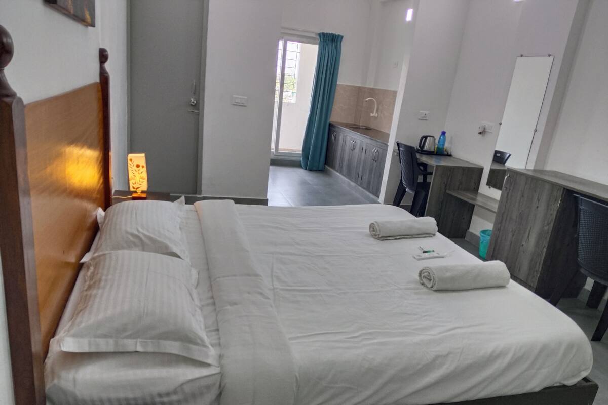 A hotel room with a large bed, a desk, a chair, and a bathroom visible through an open door.