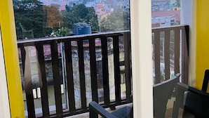 A balcony with a view of a cityscape, a table, and two chairs. - Hotel Auro Maison (Puducherry)
