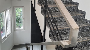 A staircase with black and white marble steps, a metal handrail, and a view of a room with a window and a door. - Hotel Auro Maison (Puducherry)