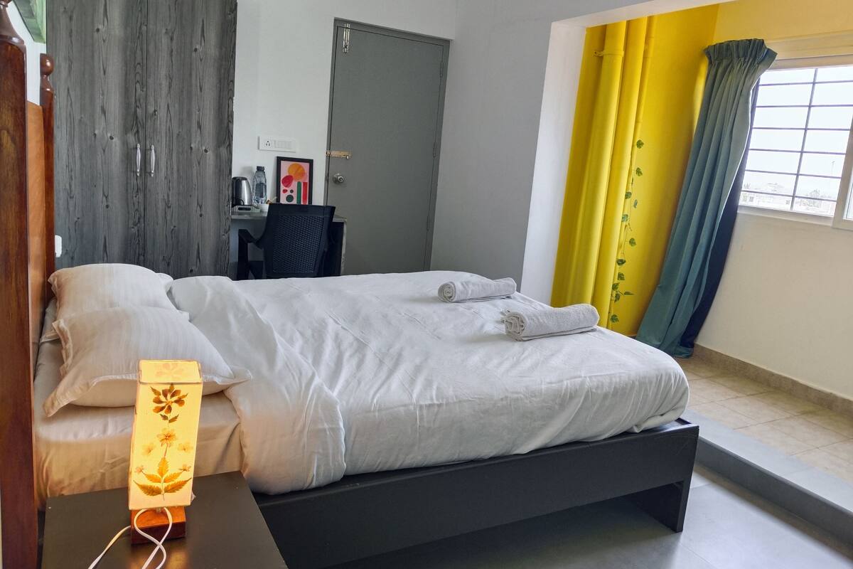 A bedroom with a bed, bedside table, lamp, and a desk with chair.