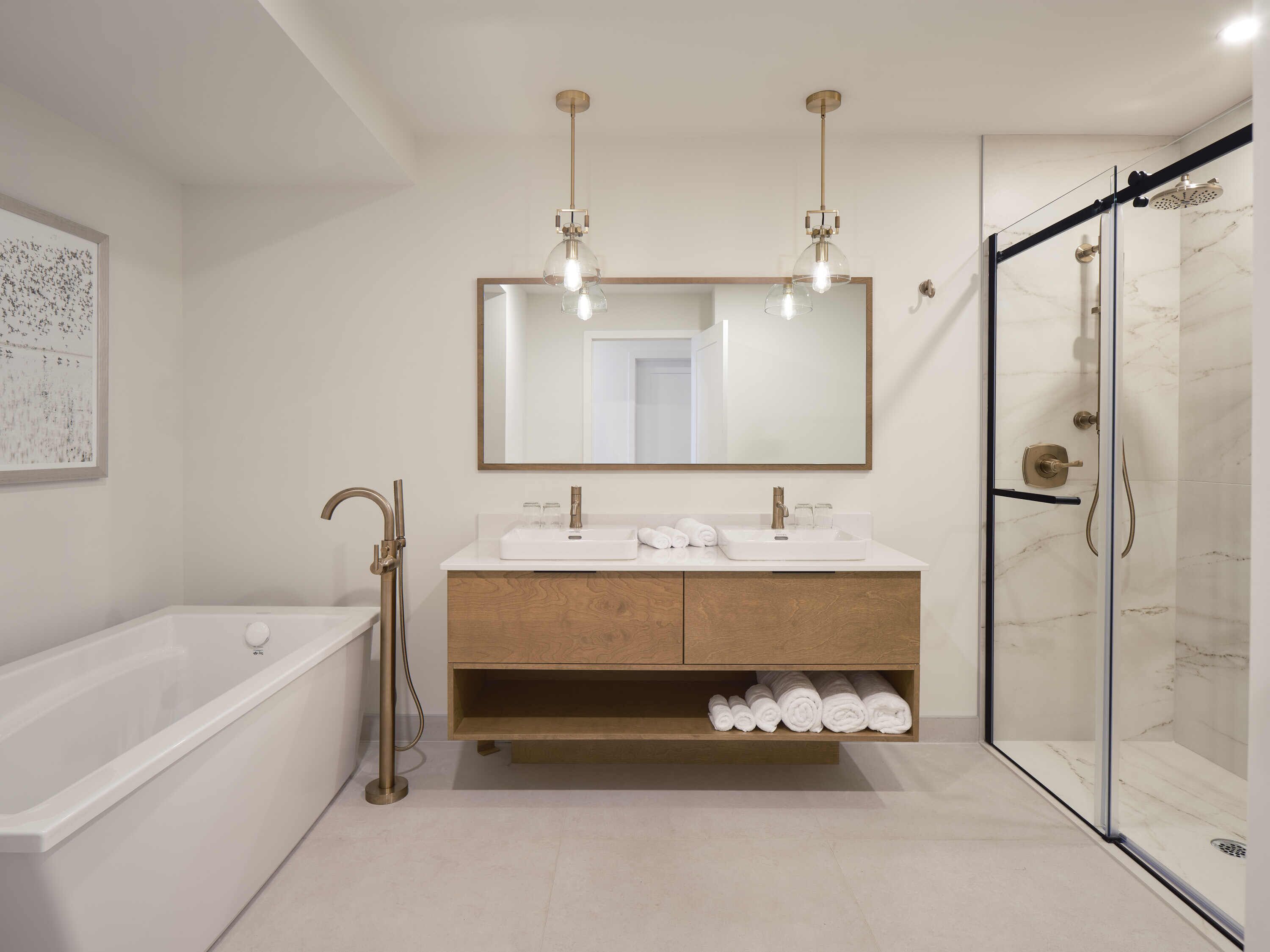 A modern bathroom with a bathtub, two sinks, a large mirror, and a glass-enclosed shower.