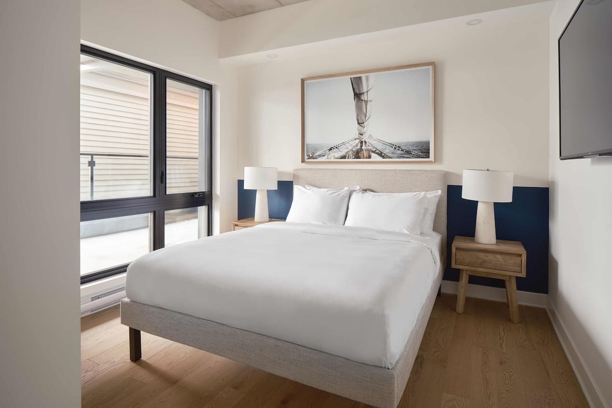 A neatly arranged hotel room with a large bed, two bedside tables with lamps, a painting above the bed, and a TV on the wall.