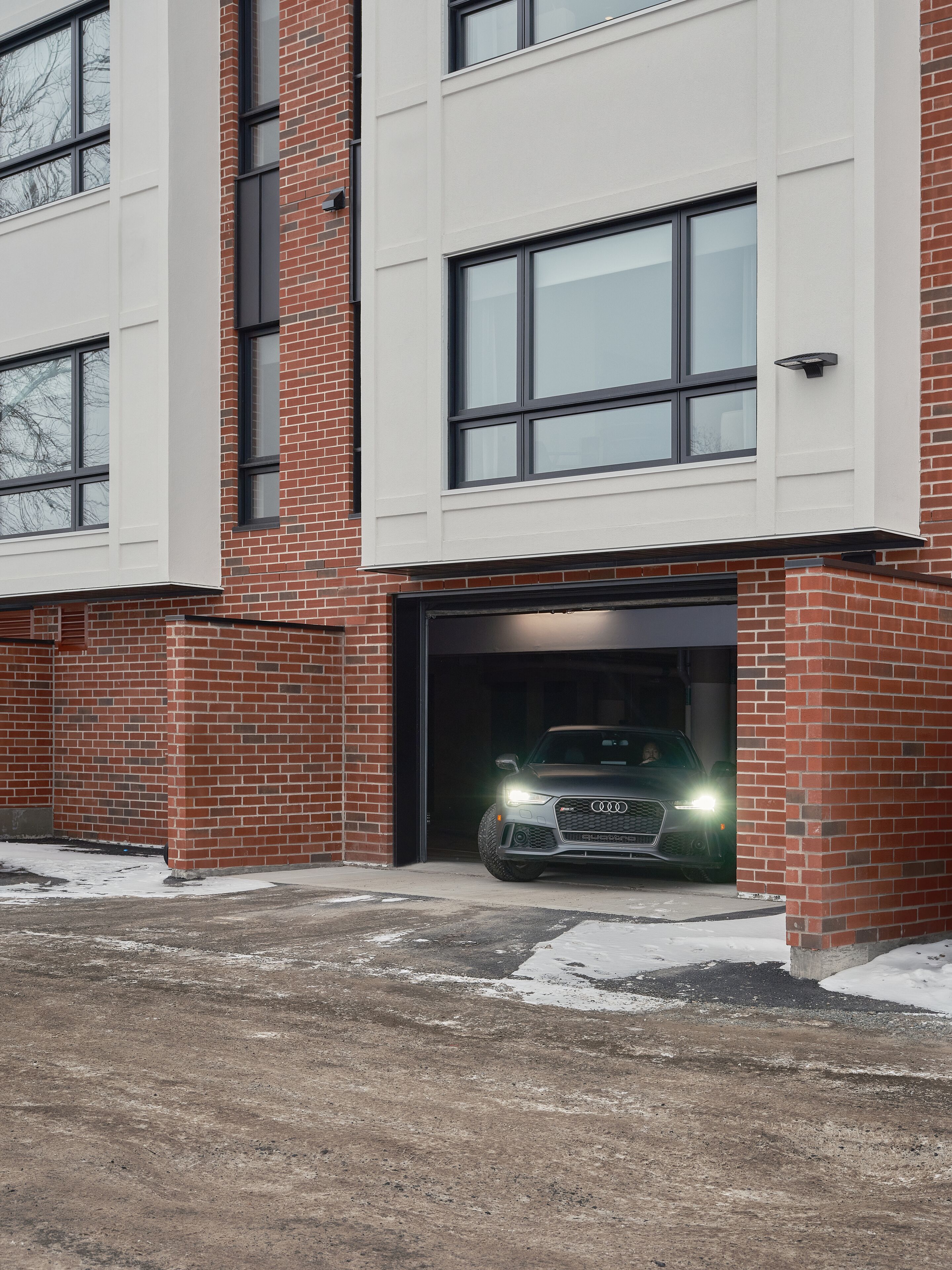 A modern building with a garage entrance, a brick facade, and a car parked inside.