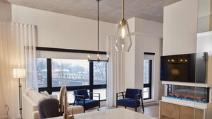 A modern kitchen with a white countertop, a built-in sink, and a large window offering a view of the city. - Quartier des Marinas - Hôtel Expérience (Magog)