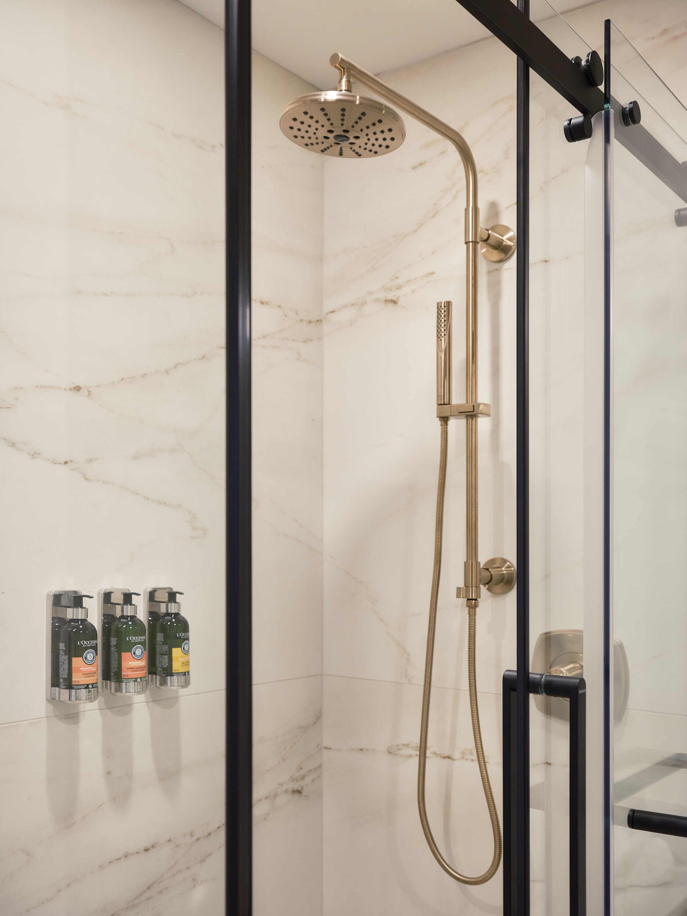 Une salle de bain moderne avec une douche à l’italienne en verre, des murs en marbre et une porte en verre.