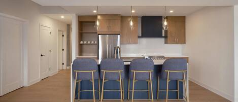 Una cocina moderna con una isla central, cuatro taburetes de bar, armarios de madera e iluminación colgante.