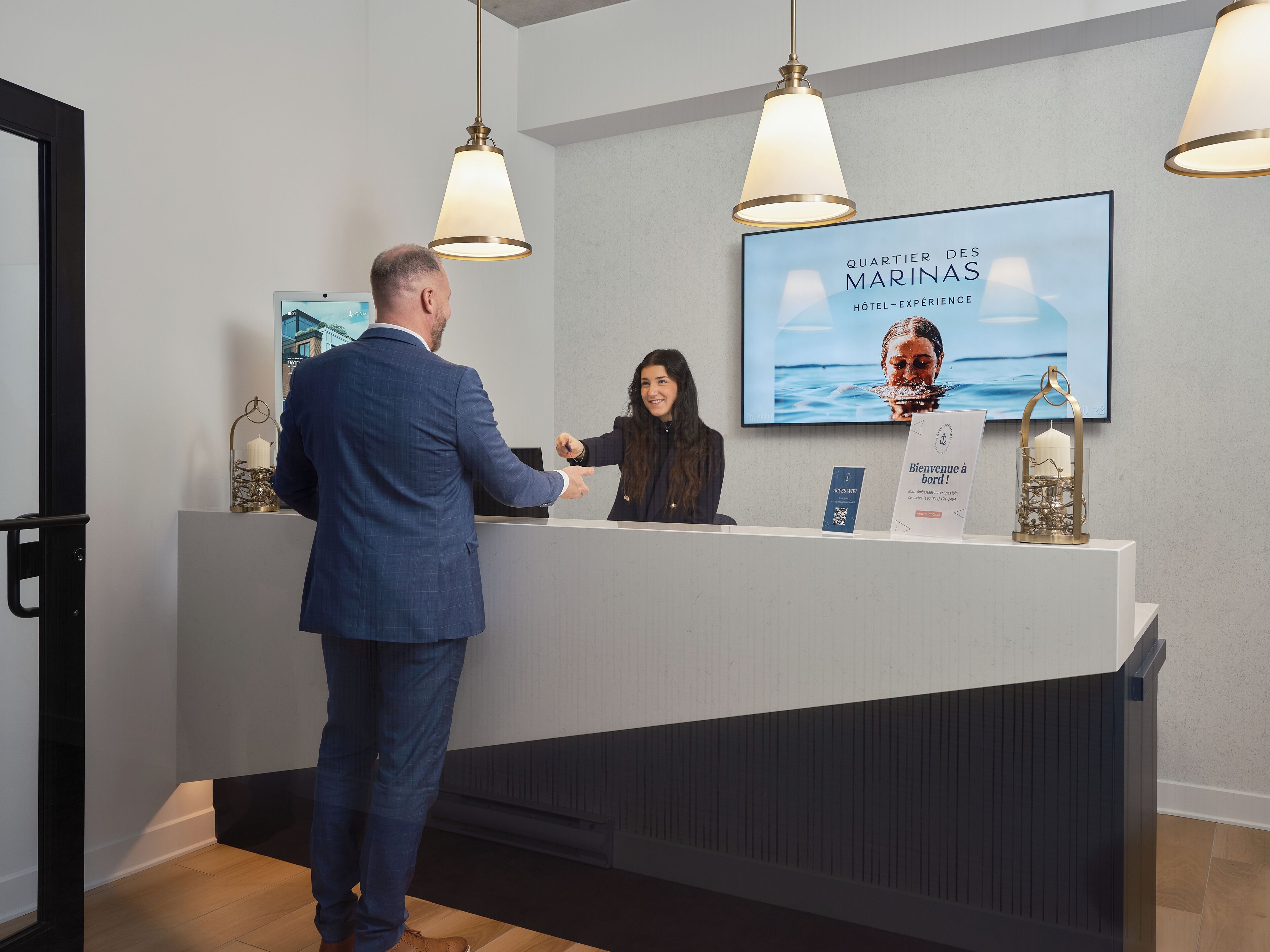 A reception desk with a large screen displaying the hotel name and a welcome sign.