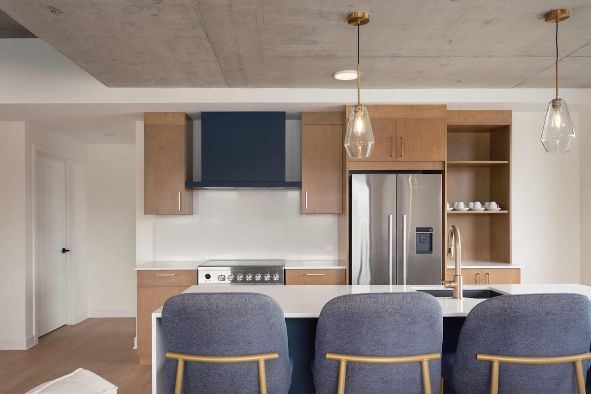 A modern kitchen with a stainless steel refrigerator, wooden cabinets, and a central island with bar stools.