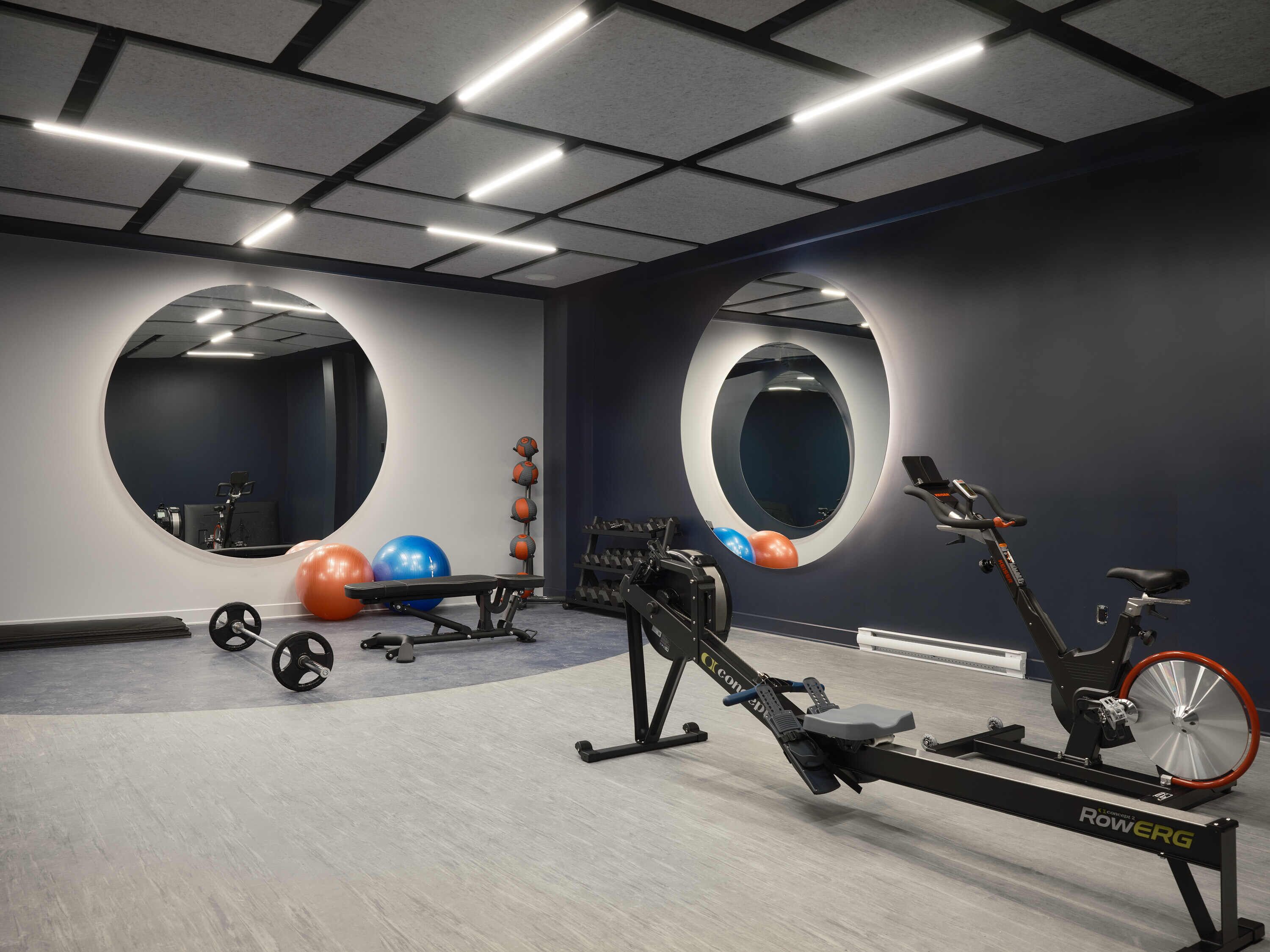 A modern gym with exercise equipment, large mirrors, and a rowing machine.