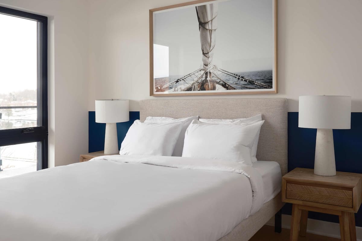 A hotel room with a large bed, two bedside tables with lamps, a framed picture on the wall, and a window with a view of the outdoors.
