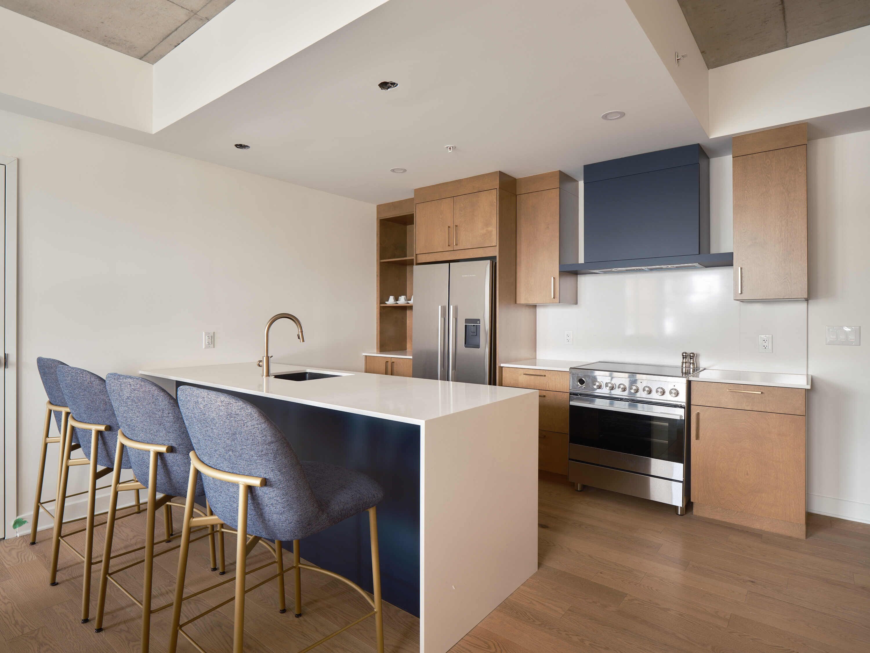 A modern kitchen with a central island, bar stools, a stainless steel refrigerator, and a built-in oven.