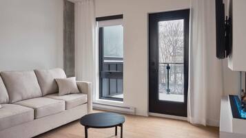 Una sala de estar moderna con un sofá, una mesita redonda y un ventanal con vistas a árboles.