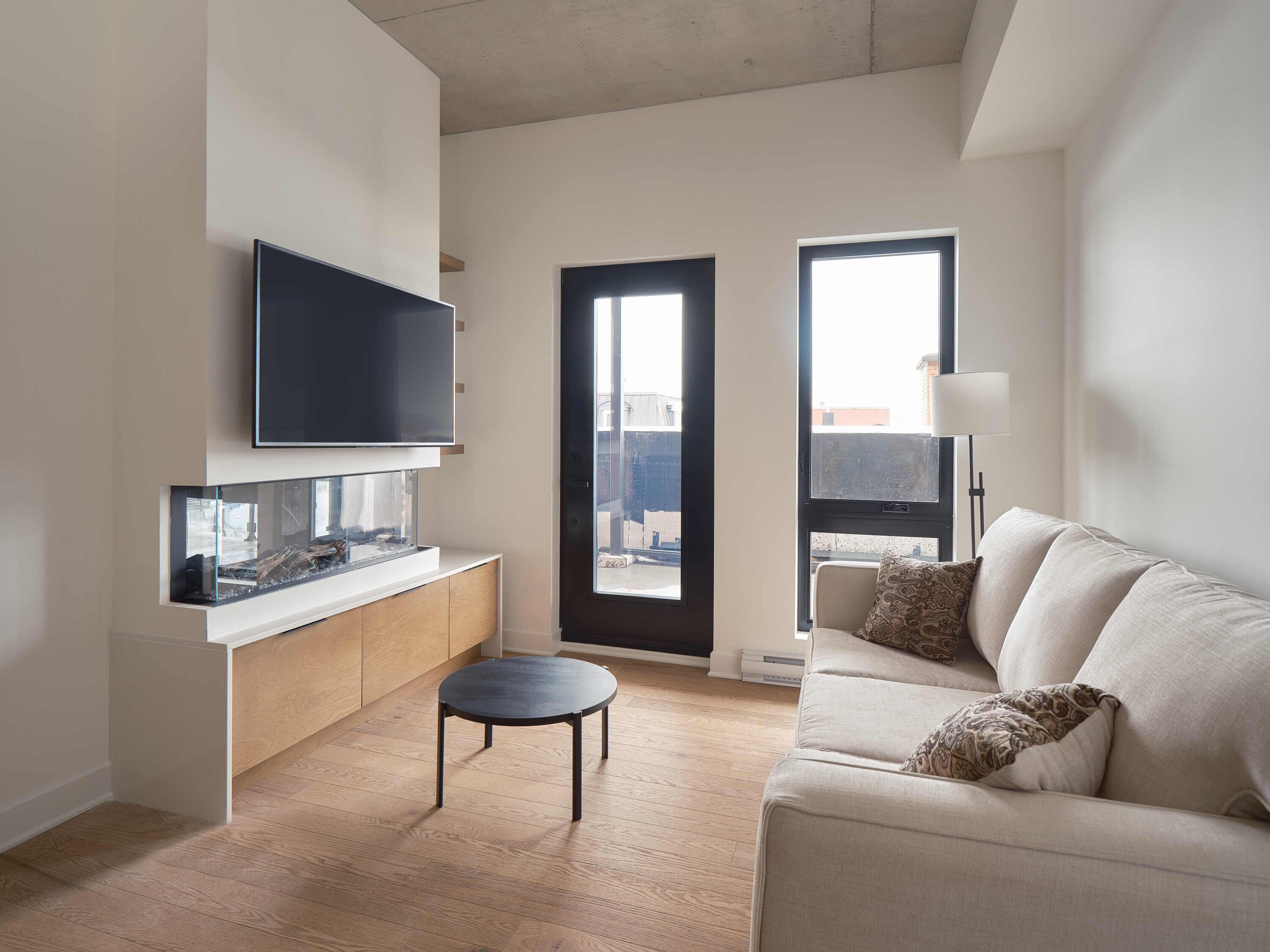 A modern living room with a flat-screen TV, a glass-top coffee table, a sofa, and a view through a door.