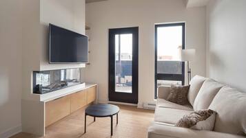 A modern living room with a flat-screen TV, a glass-top coffee table, a sofa, and a view through a door.