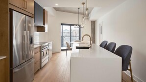 A modern kitchen with a large island, stainless steel appliances, and a dining area with chairs. - Quartier des Marinas - Hôtel Expérience (Magog)