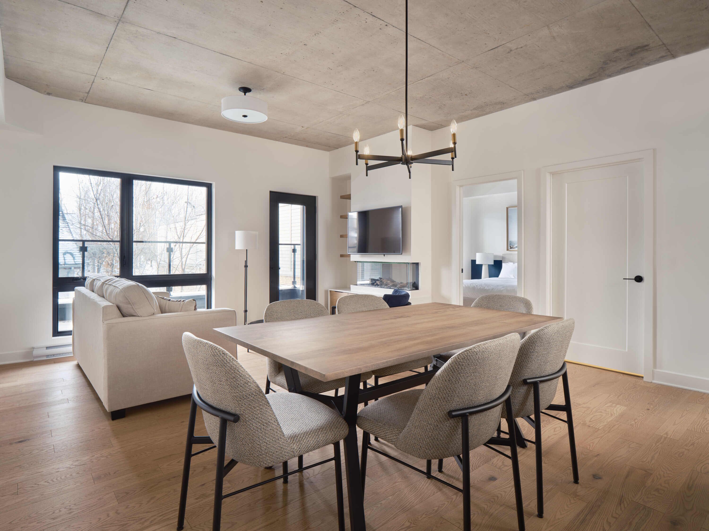 A modern dining area with a wooden table and four chairs, a sofa, a TV, and a fireplace.