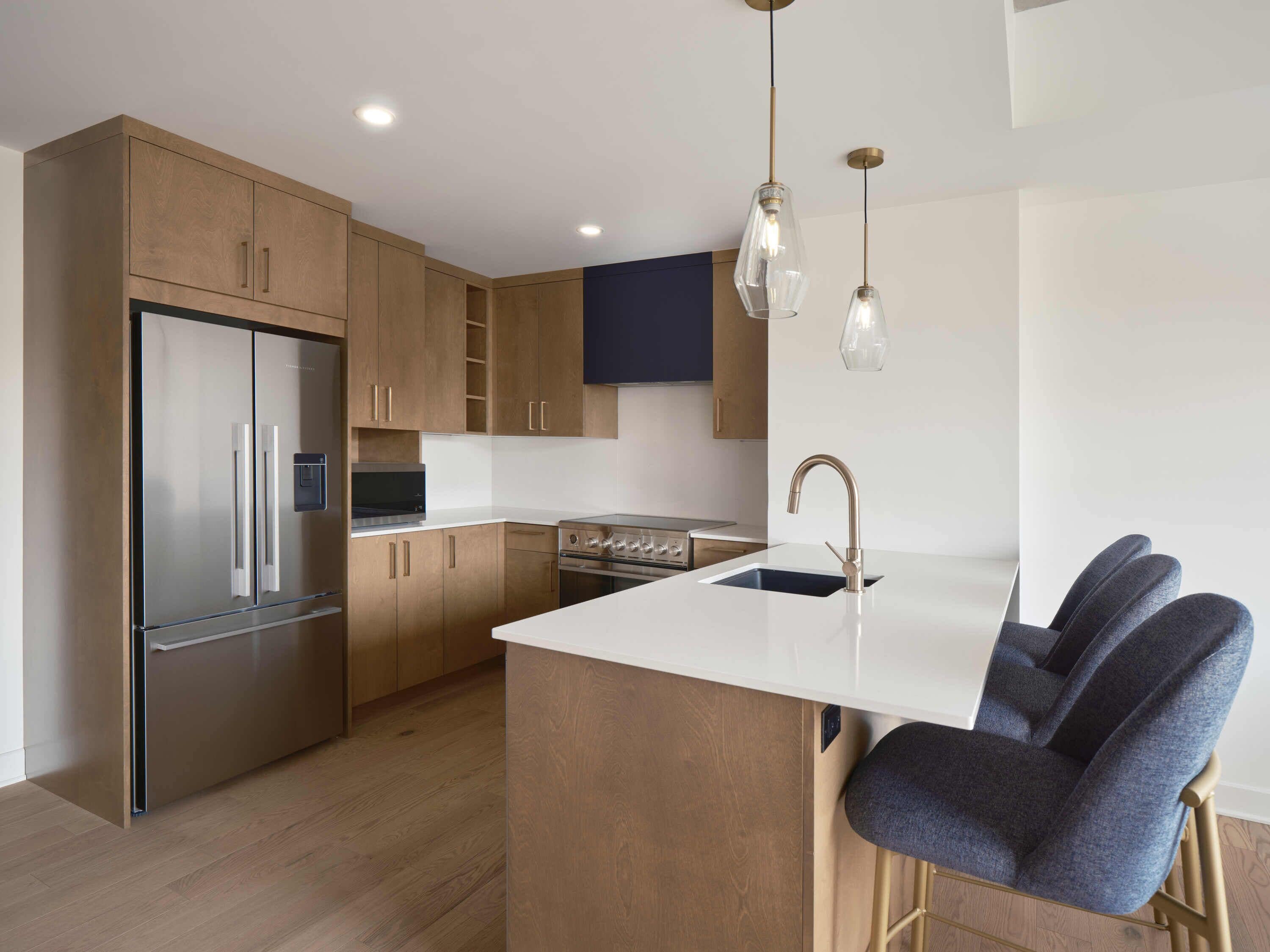 Een moderne keuken met houten kastjes, roestvrijstalen apparatuur, een centraal eiland met barkrukken en hanglampen.