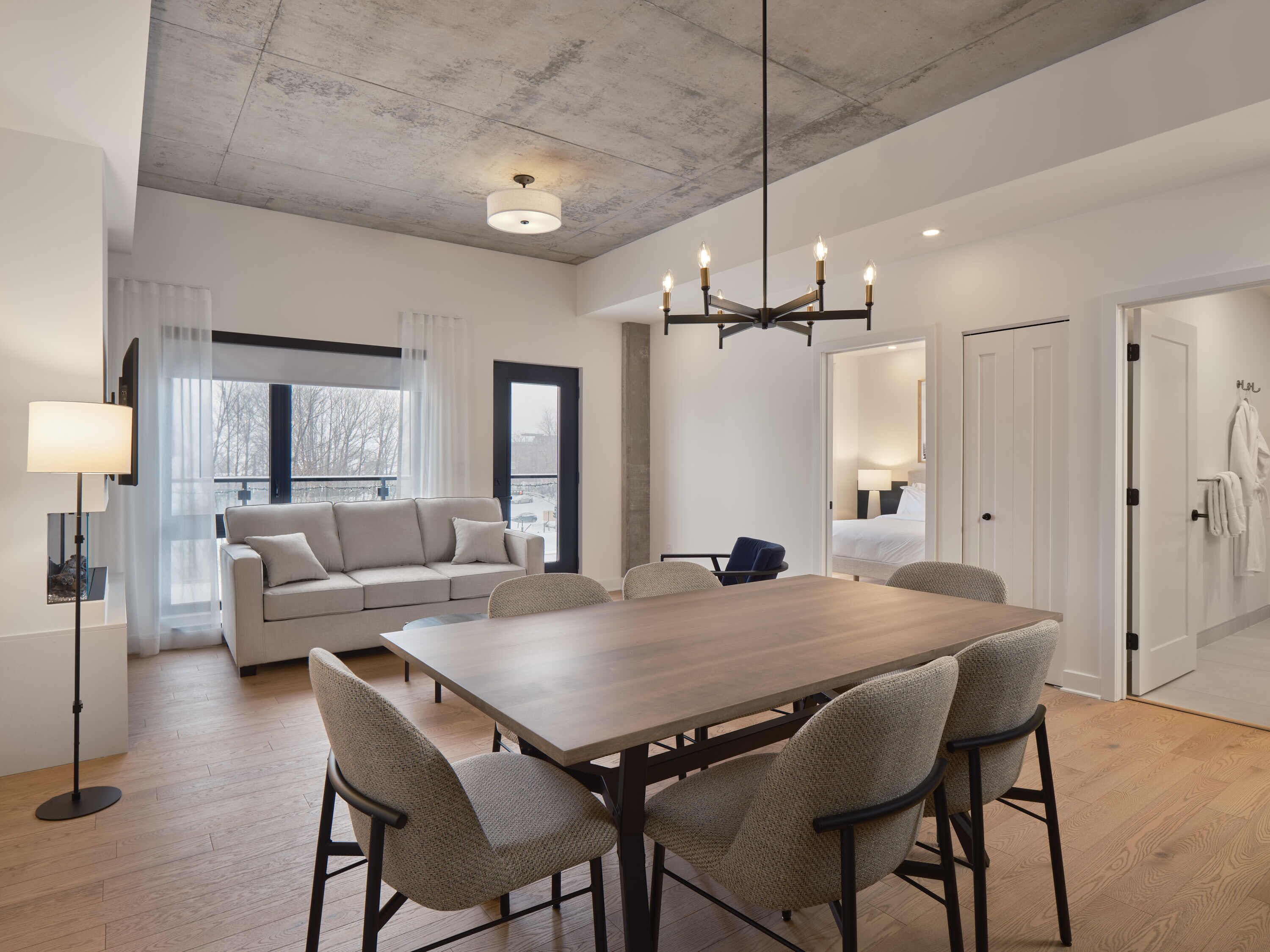 A modern hotel room with a dining area, a sofa, a chandelier, and a view of the outdoors.