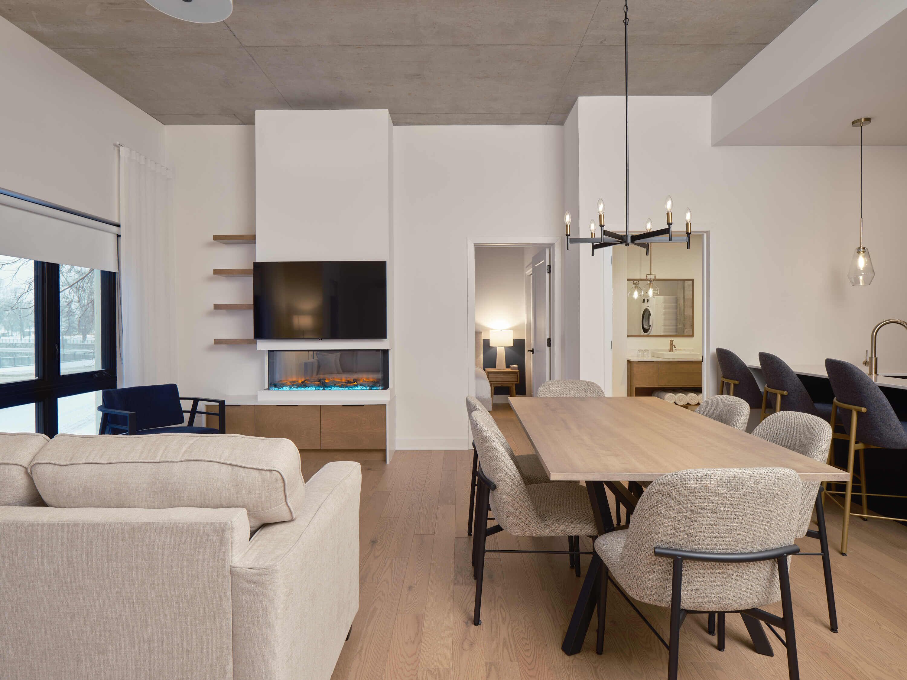 A modern living room with a sofa, a TV, a fireplace, and a dining area with chairs and a table.