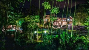 A large, multi-story building with a well-lit swimming pool area surrounded by lush greenery.
