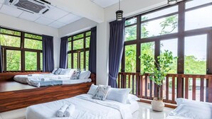 A hotel room with two beds, large windows, a balcony, and a ceiling fan.