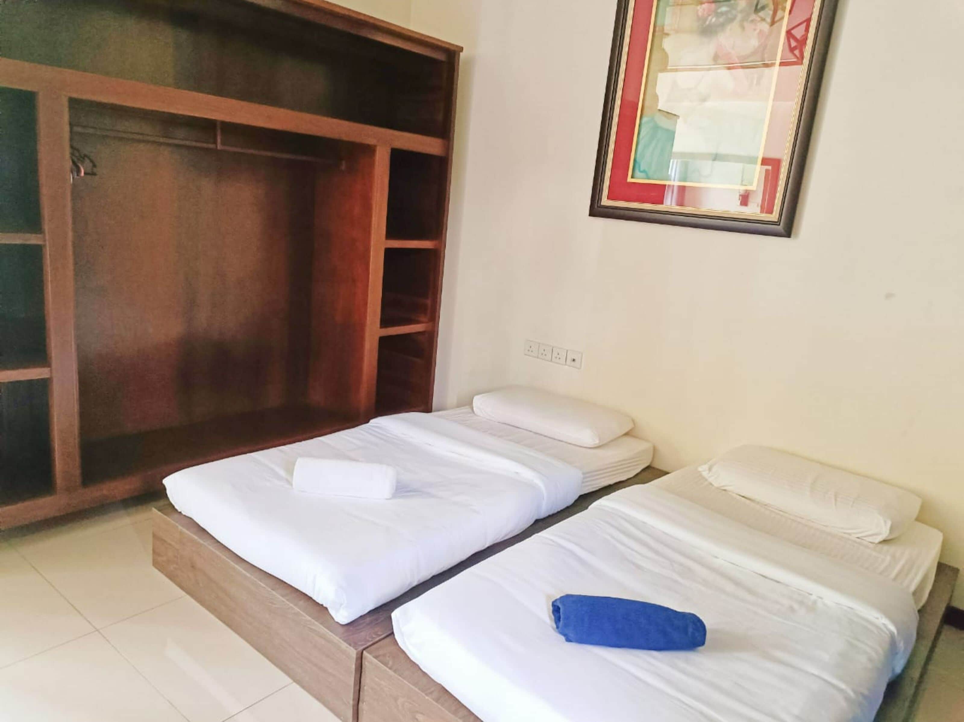 A room with two single beds, a wooden wardrobe, and a framed picture on the wall.