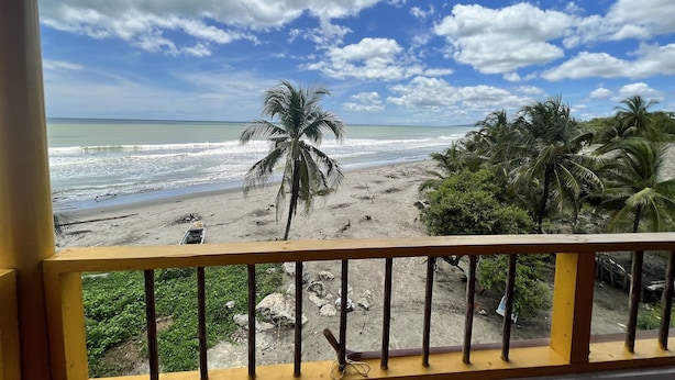 A beach view from a balcony with a railing, palm trees, and ocean waves. - Punta Antioquia Hotel (San Juan de Urabá)