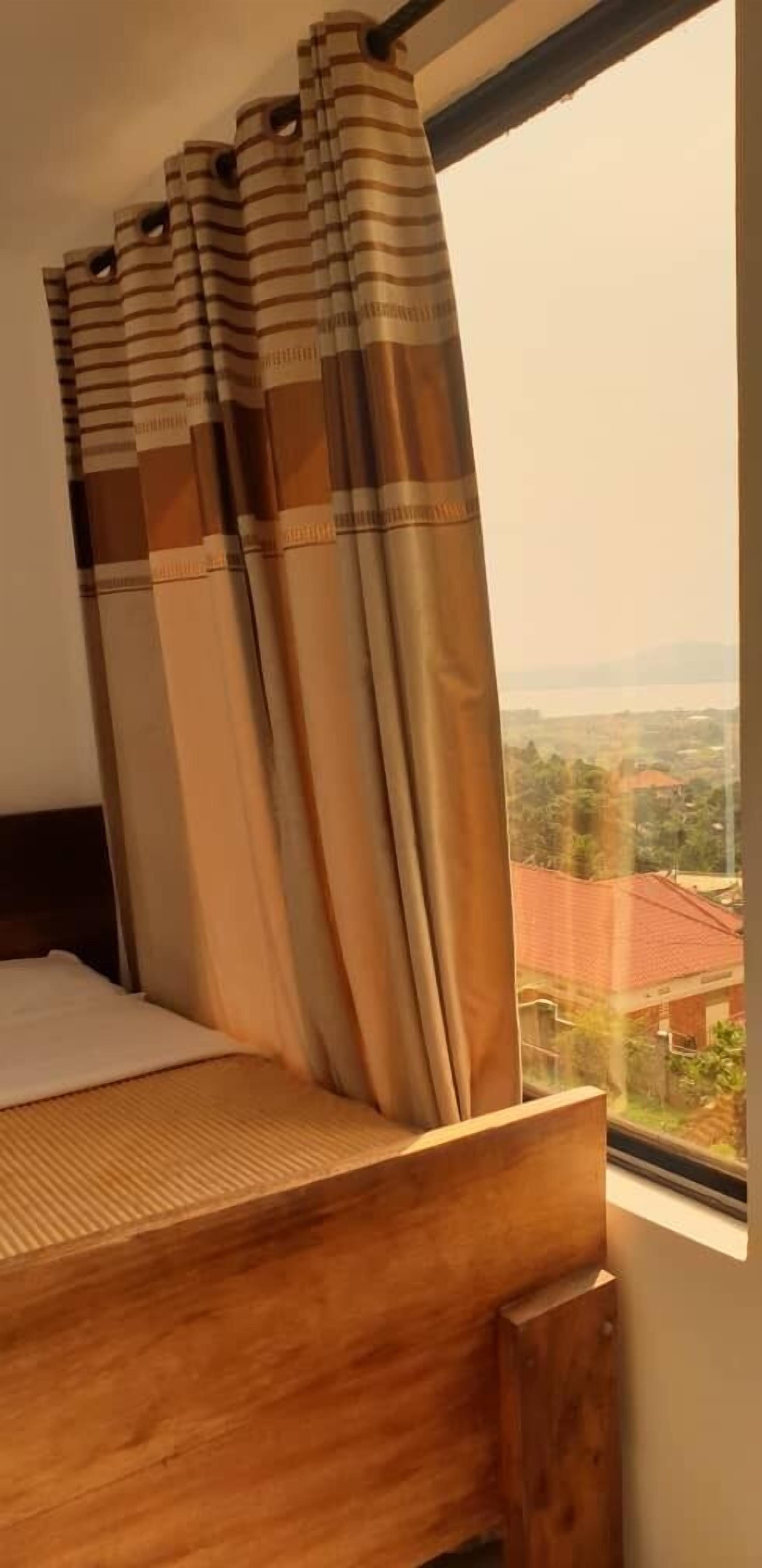 Een slaapkamer met een houten bed, beige gordijnen en uitzicht op een stadsgezicht door een raam.