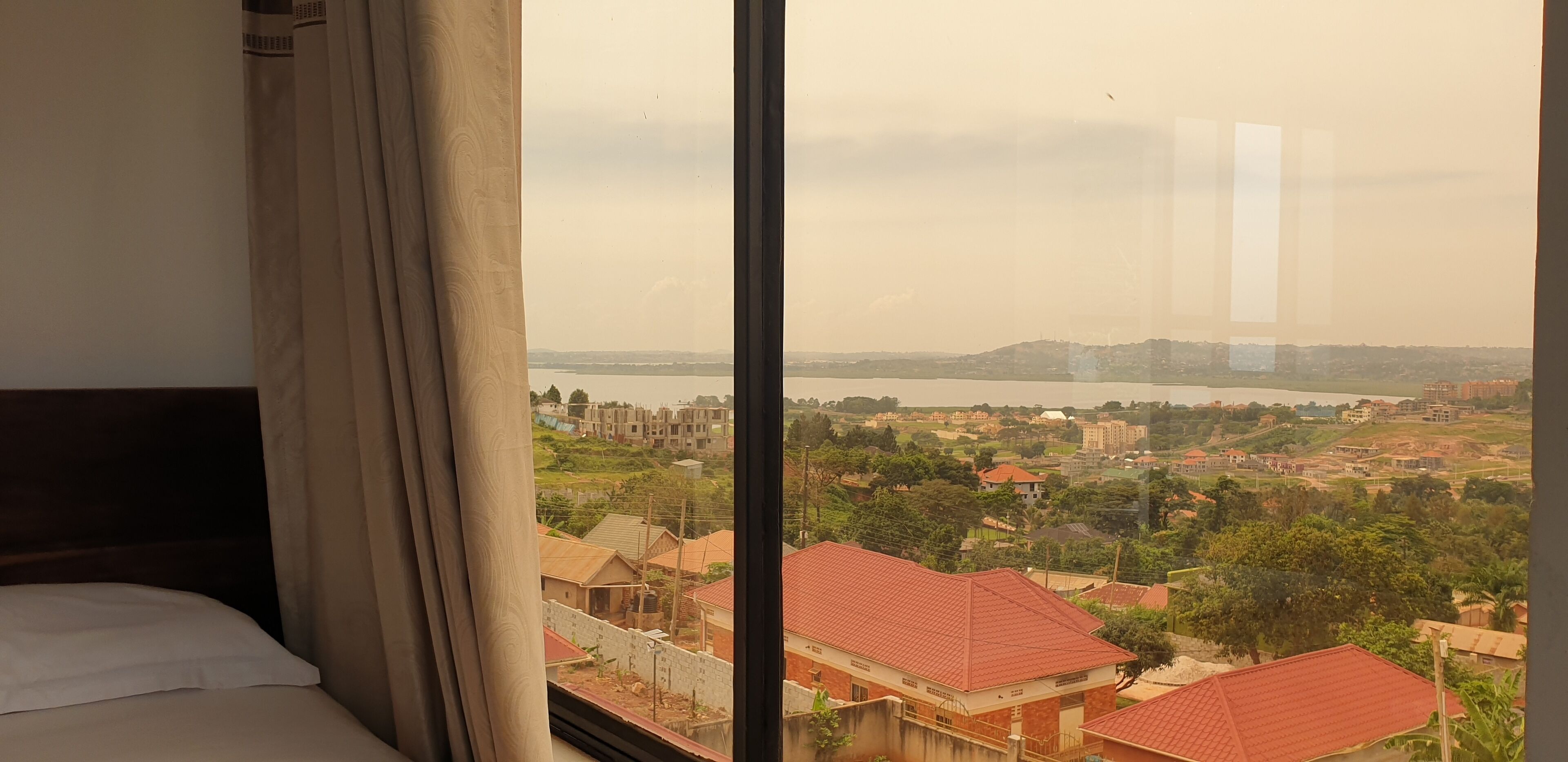 A hotel room with a large window overlooking a residential area with houses and a body of water.