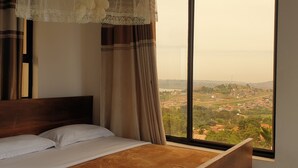 Ein Schlafzimmer mit großem Fenster, Holz-Kopfteil und Blick auf eine Stadtlandschaft.