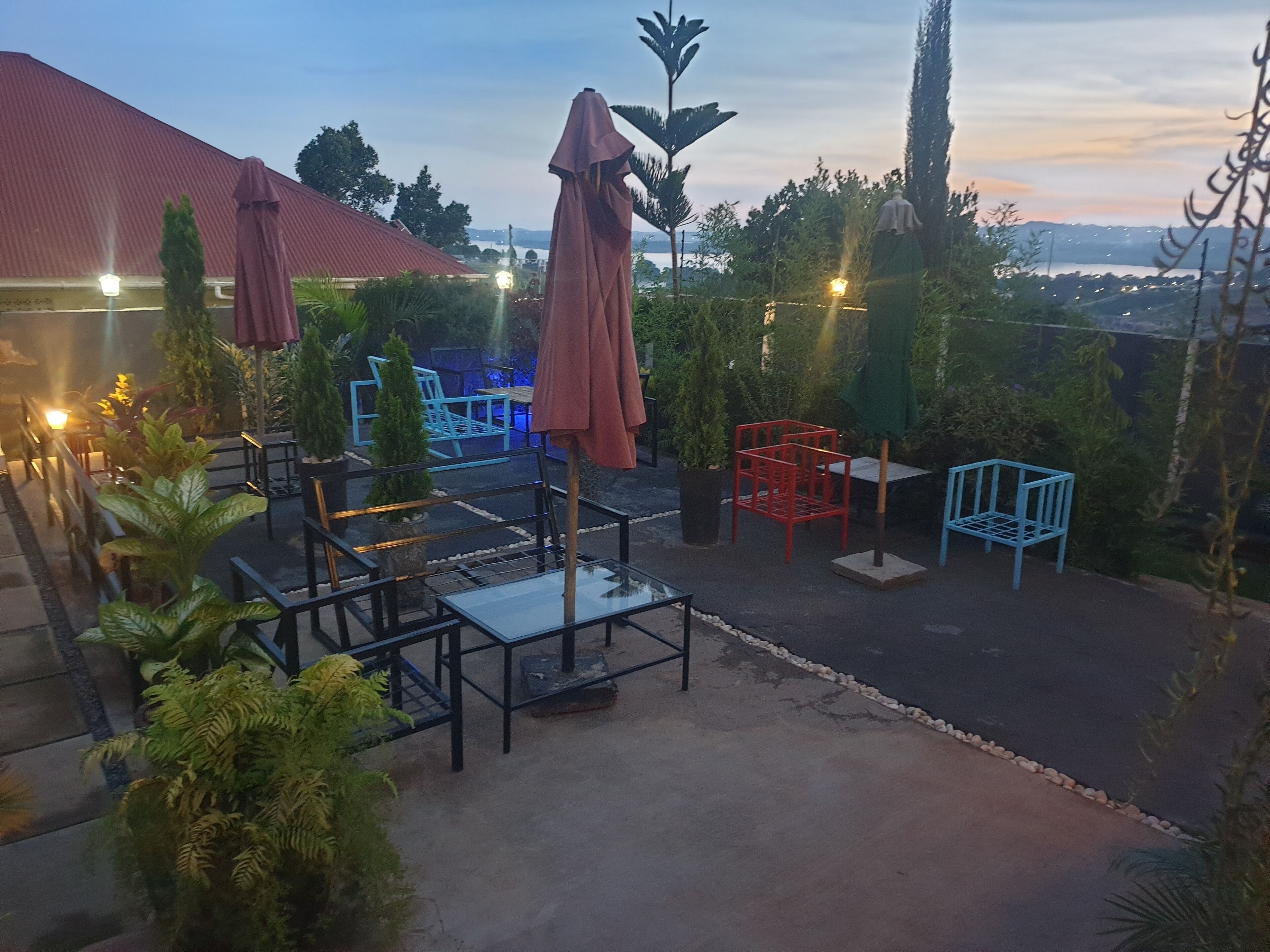 Un espace extérieur aménagé avec des tables et des chaises, entouré de plantes en pot et de parasols.