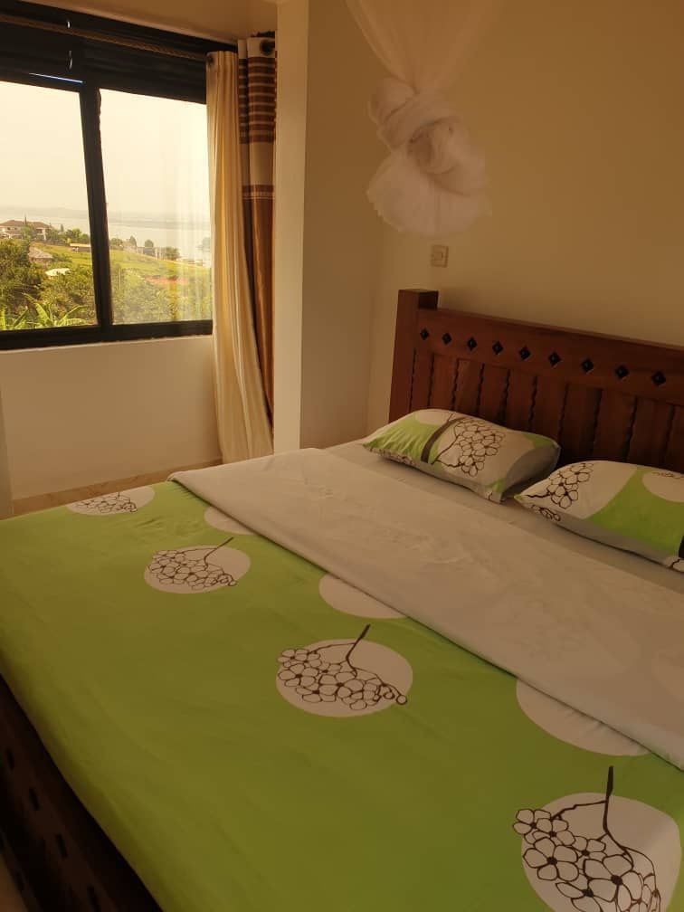 A bedroom with a large window, a bed with green bedding, and a wooden headboard.