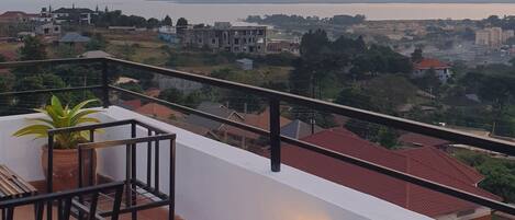 Una terraza con una mesa de vidrio, sillas y plantas en macetas, con vistas a una zona residencial con edificios y una masa de agua.