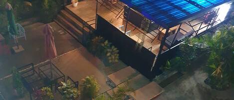 An aerial view of a rooftop with a blue-tinted structure, surrounded by greenery and a paved area.