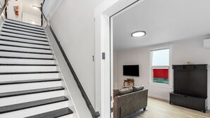 Uma escadaria leva a uma sala de estar com sofá, televisão de tela plana e janela com vista vermelha.