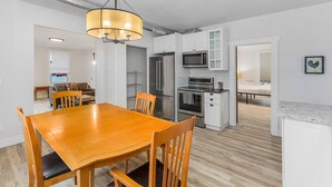A modern kitchen with white cabinets, stainless steel appliances, and a wooden dining table. - The Nighthawk Eyrie (Stanwood)
