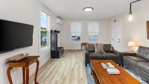 A modern living room with a flat-screen TV, a wooden coffee table, a leather sofa, and a lamp. - The Nighthawk Eyrie (Stanwood)