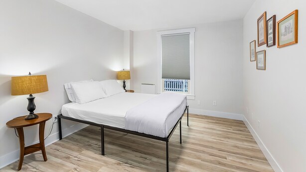 Quarto com cama, abajures, janela com persianas e quadros na parede.