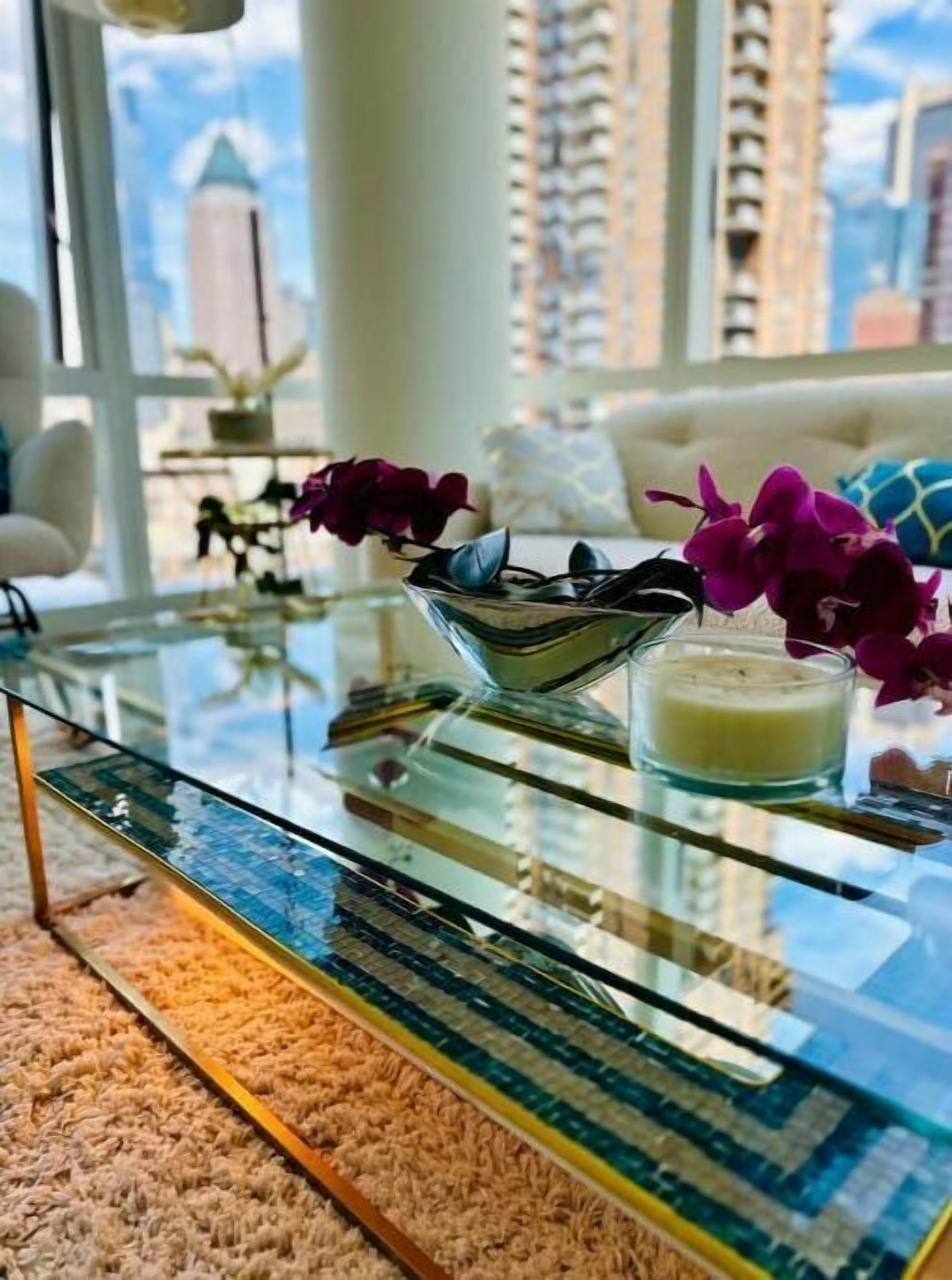 A modern living room with a glass coffee table, a candle, and purple orchids.