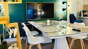A modern living room with a glass dining table, white chairs, a large flat-screen TV, and a teal accent wall. - Times Square Luxurious Massive 2bed/2bath flat,NYC (New York)