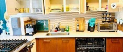 A compact kitchen with built-in cabinets, a stove, dishwasher, and a countertop with various appliances and utensils.