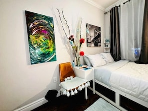 Quarto moderno com cama, mesa de cabeceira, cadeira e parede com arte abstrata em preto e branco.