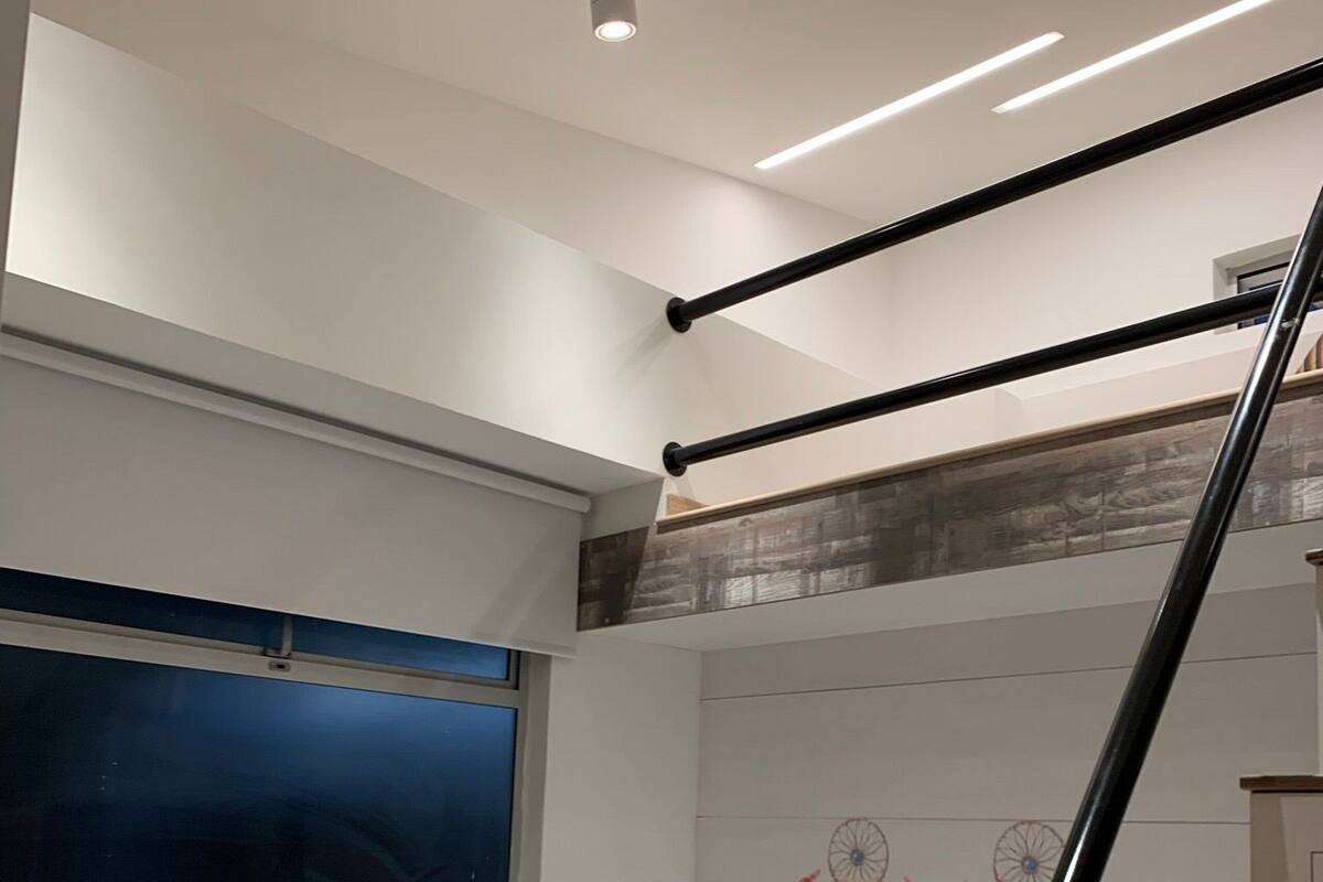 Une chambre avec un lit, une fenêtre, un mur décoré d’attrape-rêves et une rampe d’escalier.