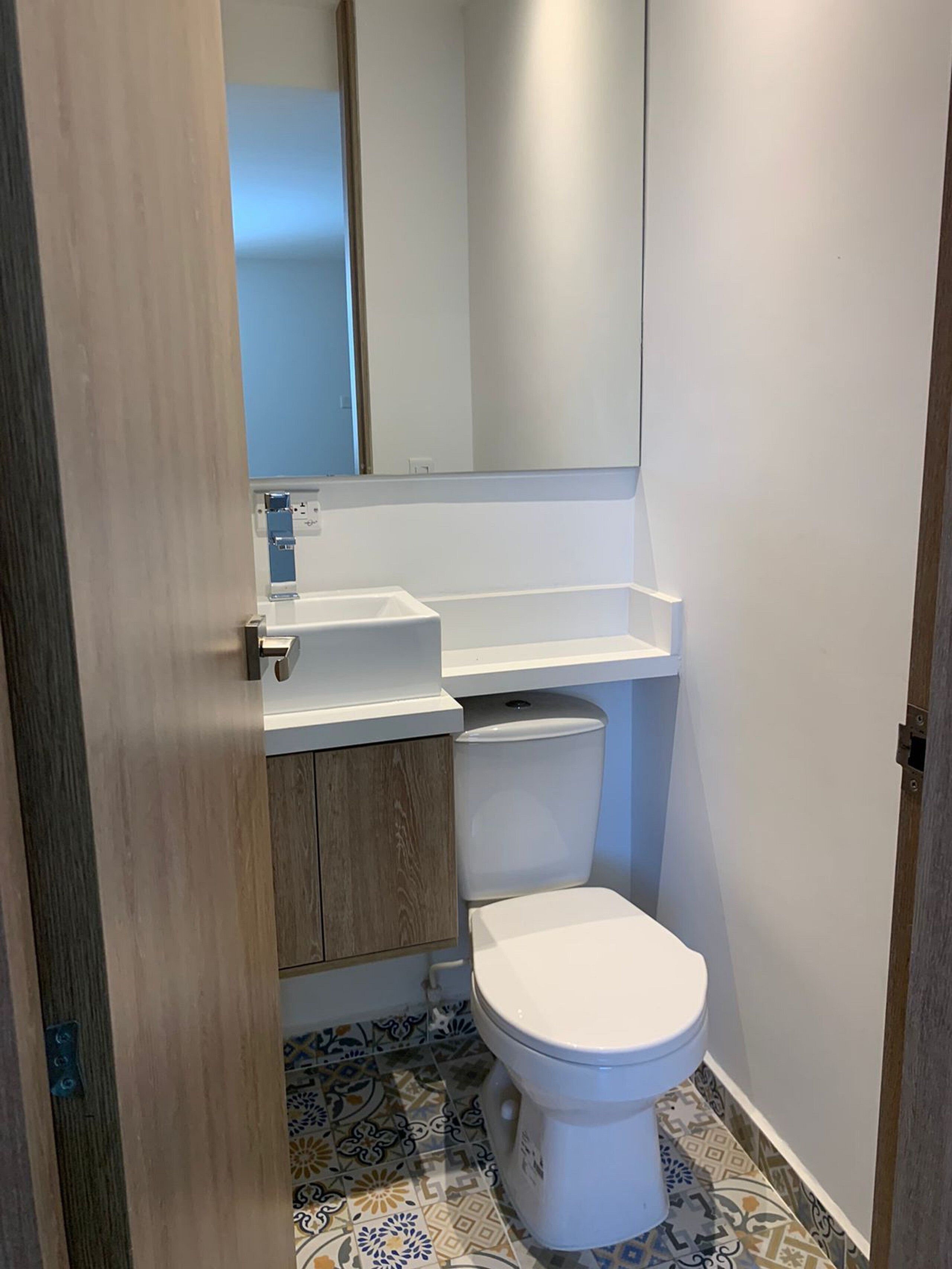 A compact bathroom with a white toilet, a wooden vanity, and a mirror above the sink.